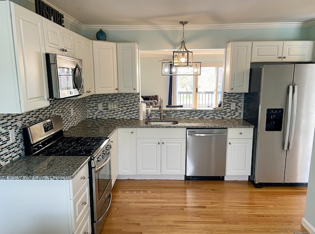 kitchen with white cabinetry, a sink, appliances with stainless steel finishes, light wood finished floors, and hanging light fixtures