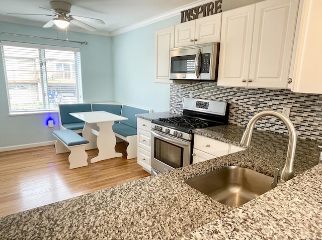 kitchen with tasteful backsplash, dark stone counters, stainless steel appliances, ceiling fan, and a sink
