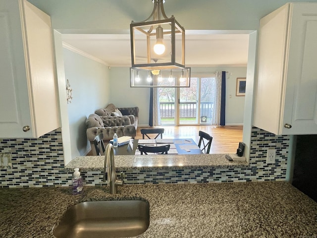 kitchen featuring tasteful backsplash, a sink, white cabinetry, open floor plan, and crown molding