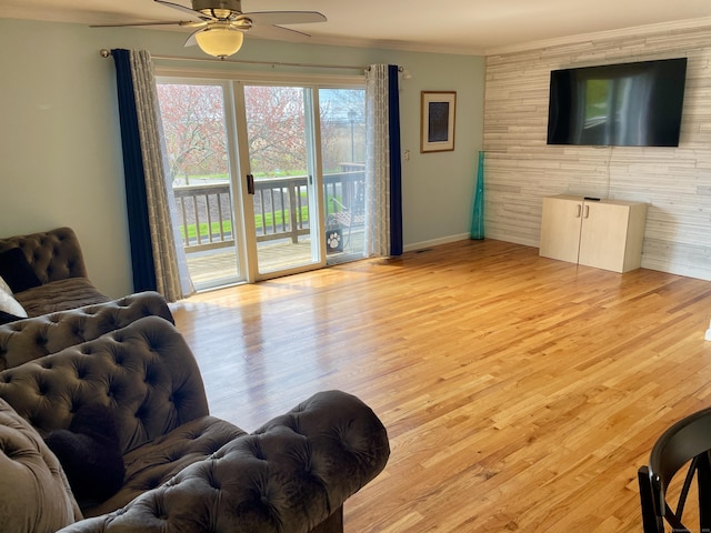 living area featuring light wood-style floors, a ceiling fan, crown molding, and baseboards