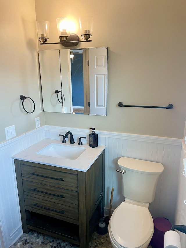 bathroom featuring toilet, a decorative wall, wainscoting, and vanity