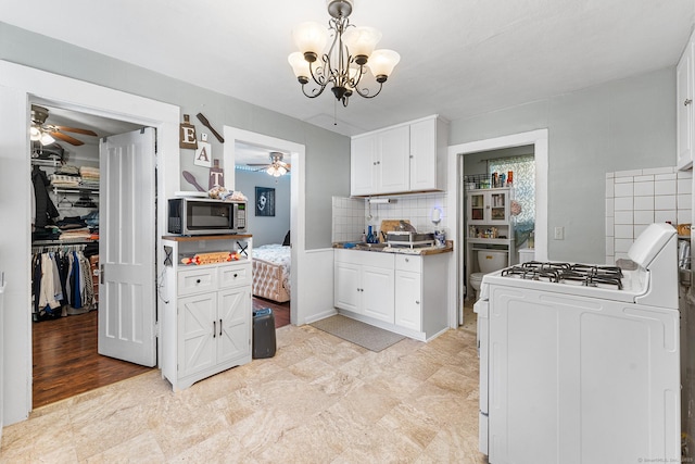 kitchen with ceiling fan with notable chandelier, stainless steel microwave, range with gas cooktop, and white cabinets