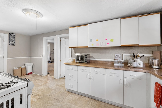 kitchen with a textured ceiling, a toaster, white cabinetry, and gas range gas stove
