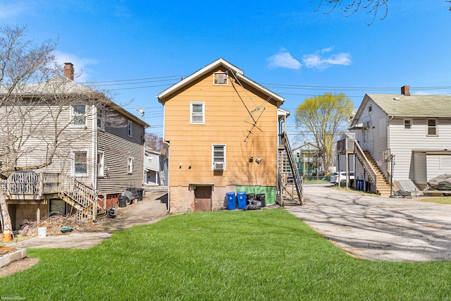 back of property featuring driveway, stairway, and a lawn