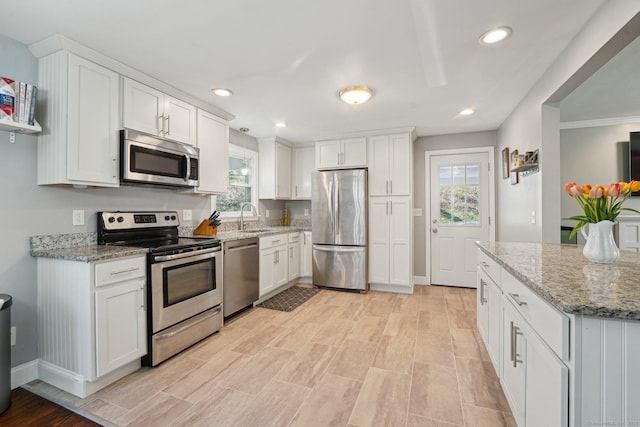 kitchen with appliances with stainless steel finishes, a sink, healthy amount of natural light, white cabinets, and recessed lighting
