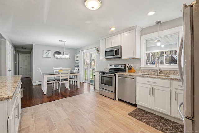 kitchen with stainless steel appliances, a sink, white cabinets, decorative light fixtures, and light stone counters