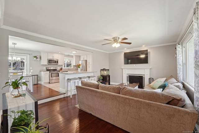 living room featuring healthy amount of natural light, wood finished floors, a brick fireplace, a ceiling fan, and crown molding