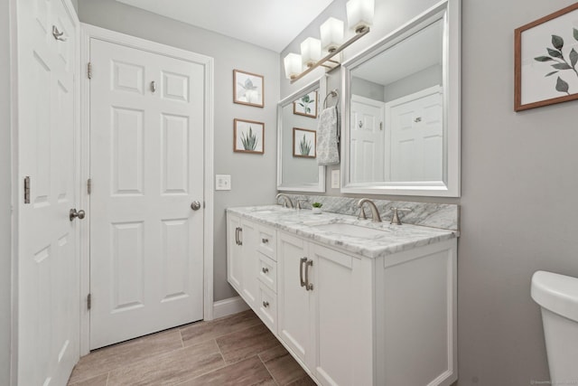 bathroom with toilet, double vanity, and wood finished floors
