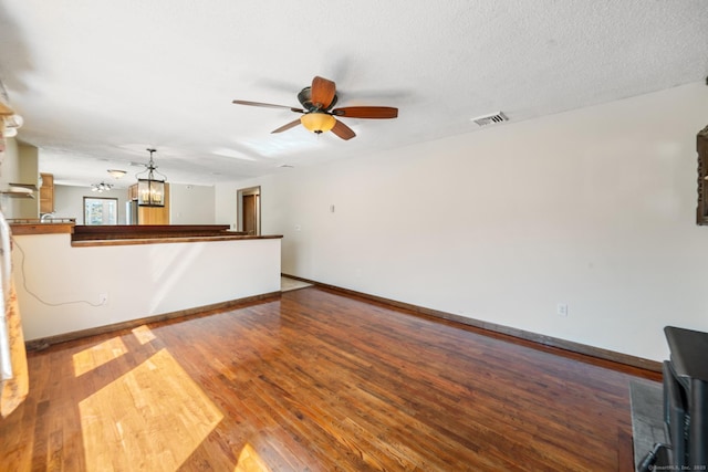 unfurnished living room featuring visible vents, ceiling fan with notable chandelier, a textured ceiling, wood finished floors, and baseboards