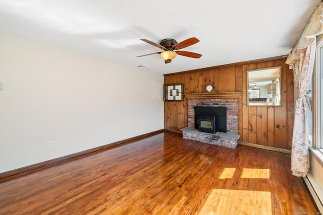 unfurnished living room featuring wooden walls, a ceiling fan, wood finished floors, baseboards, and baseboard heating