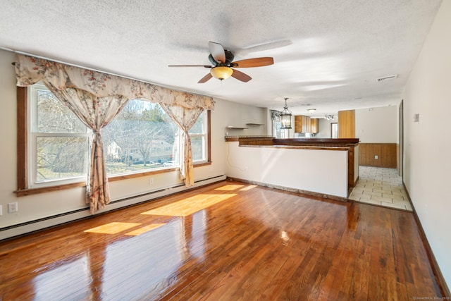 unfurnished living room featuring visible vents, hardwood / wood-style flooring, a textured ceiling, ceiling fan with notable chandelier, and baseboard heating