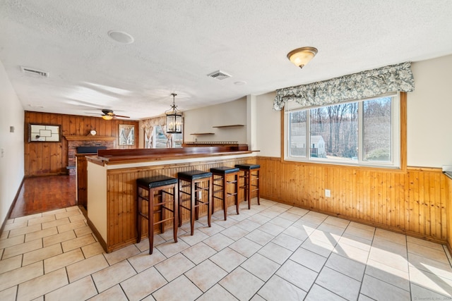 kitchen featuring wooden walls, visible vents, a textured ceiling, and a ceiling fan
