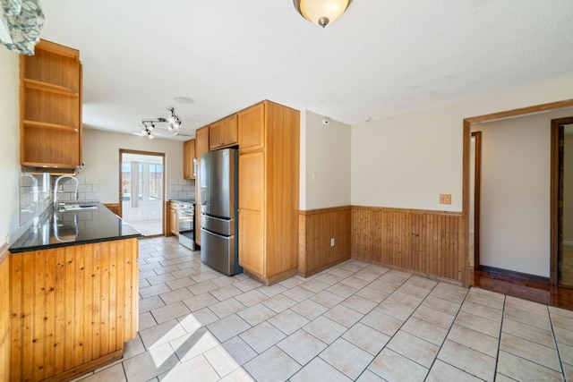 kitchen with wooden walls, a sink, stainless steel appliances, wainscoting, and backsplash