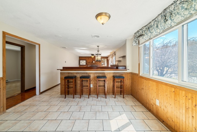 kitchen featuring visible vents, a kitchen breakfast bar, wooden walls, light tile patterned flooring, and wainscoting