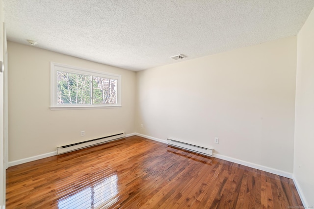 empty room featuring visible vents, a baseboard heating unit, hardwood / wood-style floors, baseboards, and baseboard heating