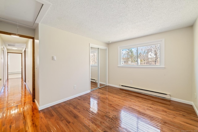 unfurnished bedroom featuring a textured ceiling, a closet, wood-type flooring, baseboards, and baseboard heating