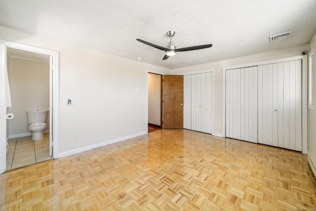 unfurnished bedroom with visible vents, baseboards, multiple closets, a textured ceiling, and ensuite bath