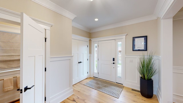 entryway with a decorative wall, ornamental molding, light wood finished floors, and wainscoting
