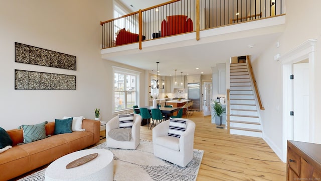 living area featuring baseboards, stairs, a towering ceiling, and light wood finished floors