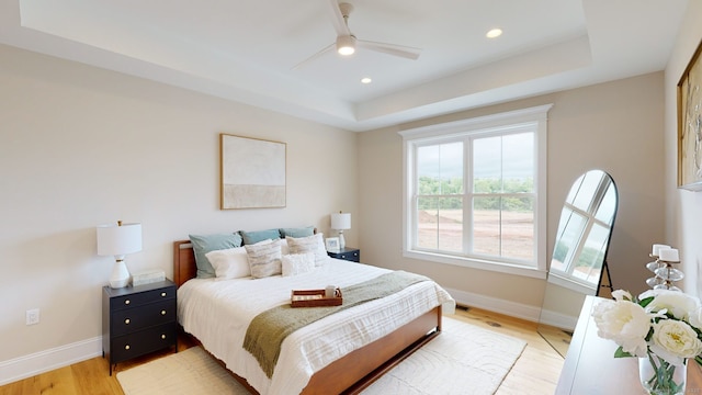 bedroom featuring baseboards, a tray ceiling, light wood-style flooring, and recessed lighting
