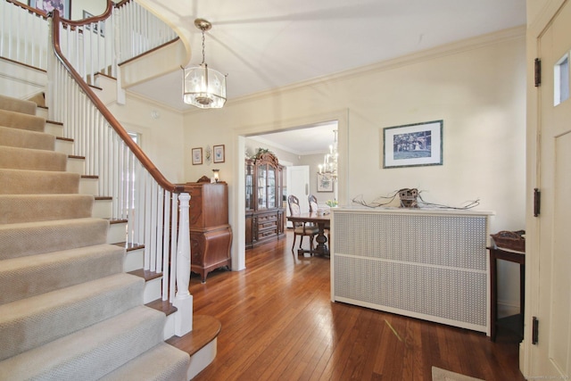 foyer featuring dark wood-type flooring, crown molding, stairway, and an inviting chandelier