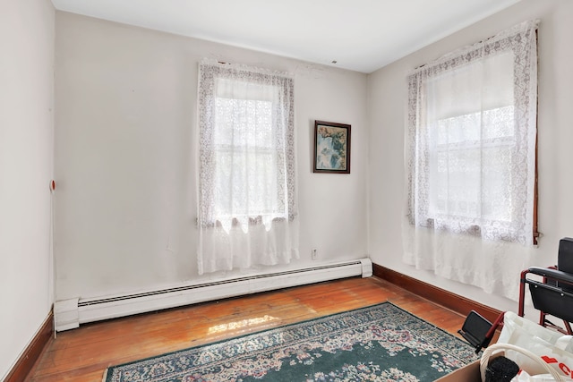 sitting room featuring baseboards, a baseboard heating unit, and wood finished floors