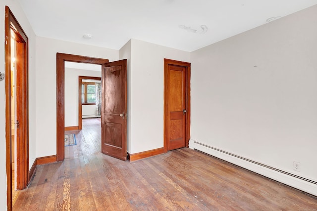 empty room featuring baseboards, a baseboard heating unit, and hardwood / wood-style floors