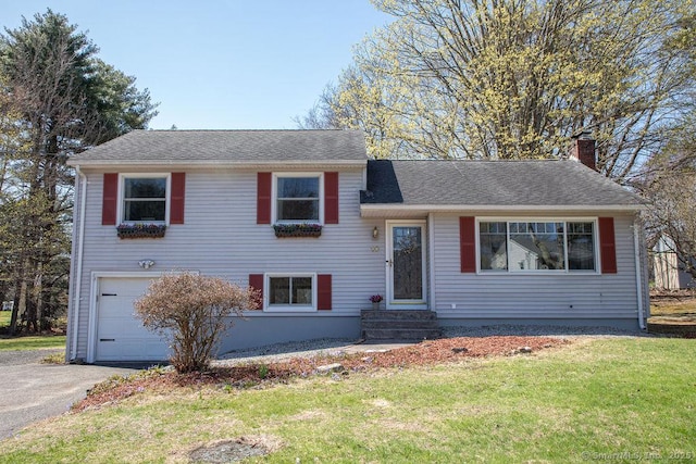 split level home with a front lawn, a chimney, entry steps, an attached garage, and driveway