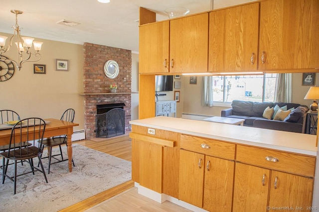 kitchen featuring a brick fireplace, light countertops, light wood finished floors, open floor plan, and an inviting chandelier