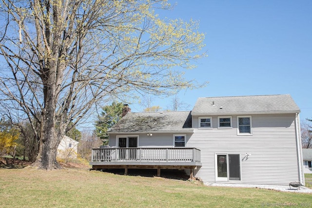 back of house featuring a lawn, roof with shingles, a wooden deck, and a chimney