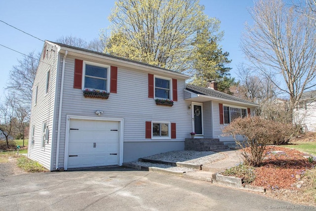 split level home featuring a garage, a chimney, and driveway