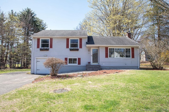split level home featuring a garage, a front yard, entry steps, a chimney, and driveway