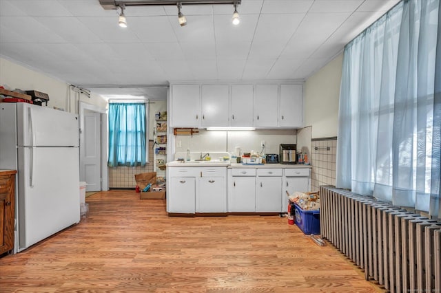 kitchen featuring radiator, light wood finished floors, freestanding refrigerator, a sink, and white cabinets