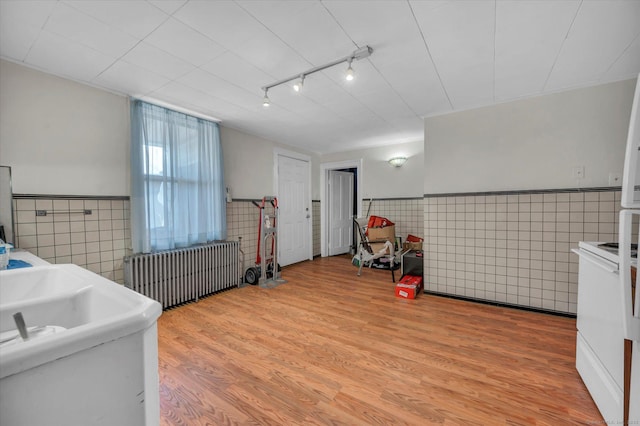 laundry area featuring tile walls, radiator heating unit, light wood finished floors, and wainscoting