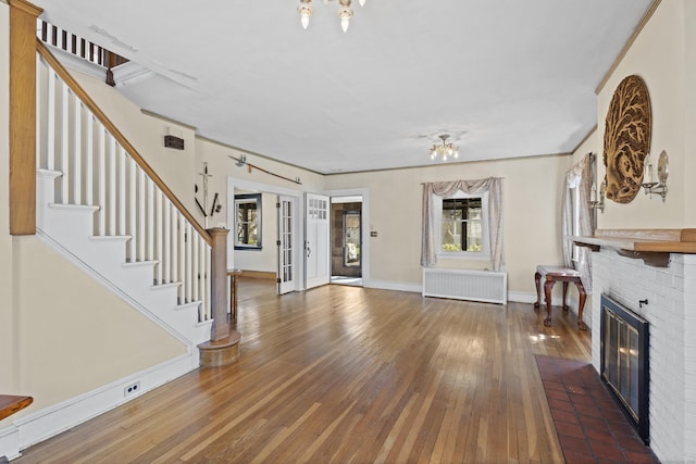 1228 Wells Pl, Stratford, CT 06615 - unfurnished living room featuring radiator, hardwood / wood-style floors, a brick fireplace, stairs, and baseboards
