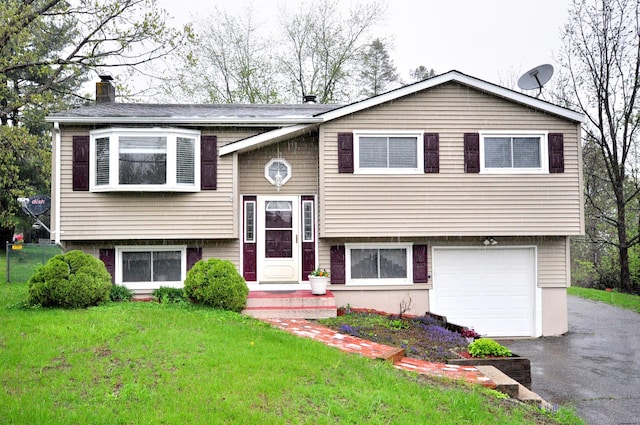 raised ranch featuring a garage, a chimney, a front yard, and asphalt driveway