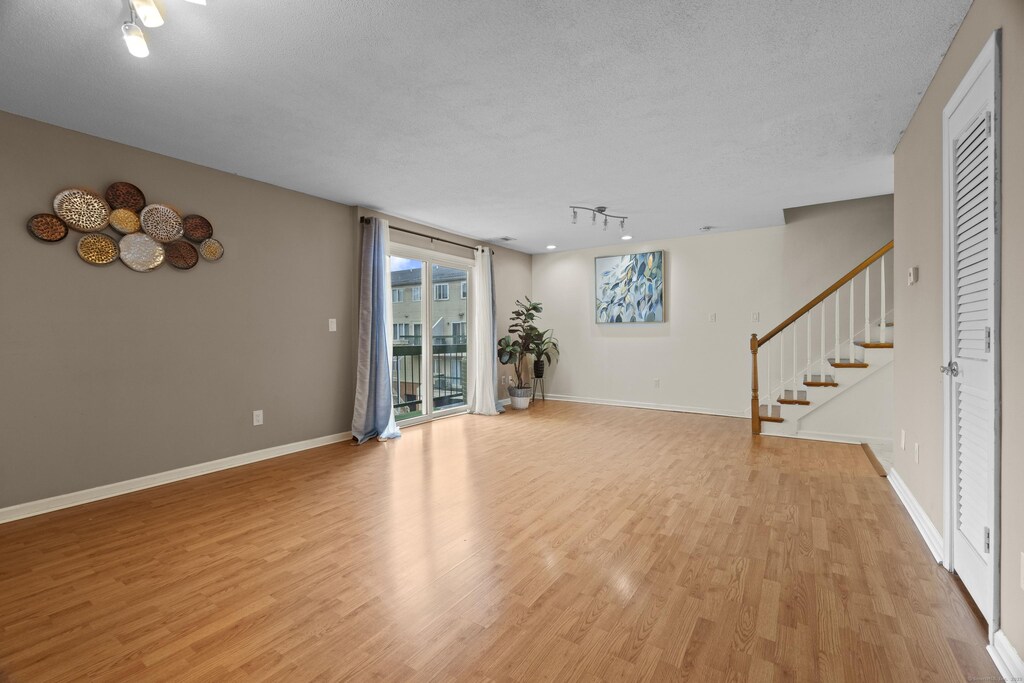 unfurnished living room featuring baseboards, light wood-type flooring, stairway, and a textured ceiling