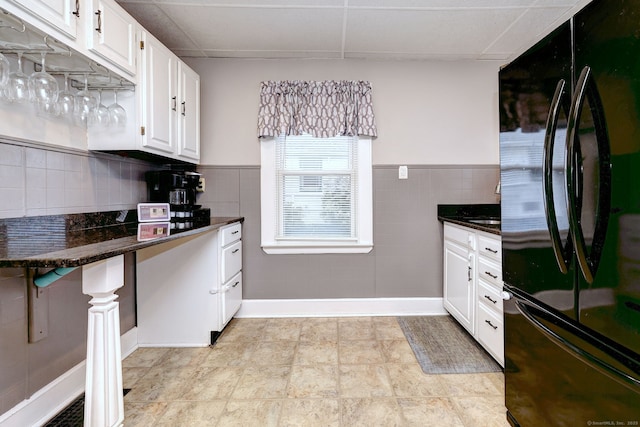 kitchen featuring tile walls, white cabinets, dark stone countertops, wainscoting, and freestanding refrigerator