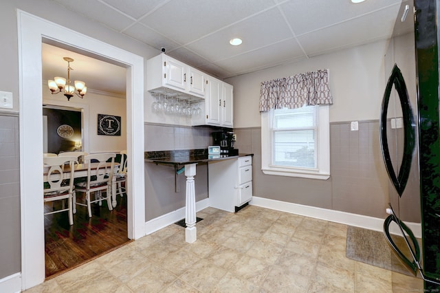 kitchen featuring white cabinets, dark countertops, an inviting chandelier, a paneled ceiling, and freestanding refrigerator