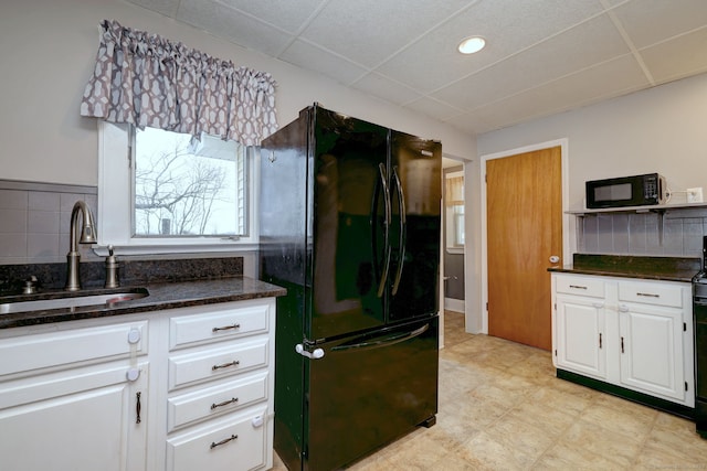 kitchen featuring dark stone counters, a sink, white cabinets, black appliances, and a paneled ceiling