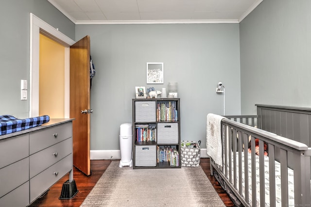bedroom with a nursery area, baseboards, ornamental molding, and dark wood-style flooring