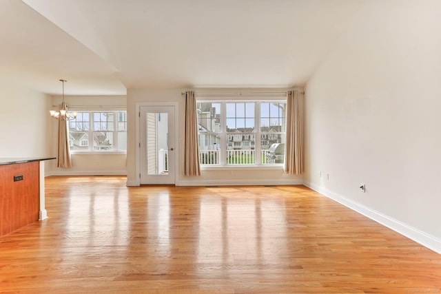 unfurnished living room featuring light wood finished floors, a notable chandelier, and baseboards