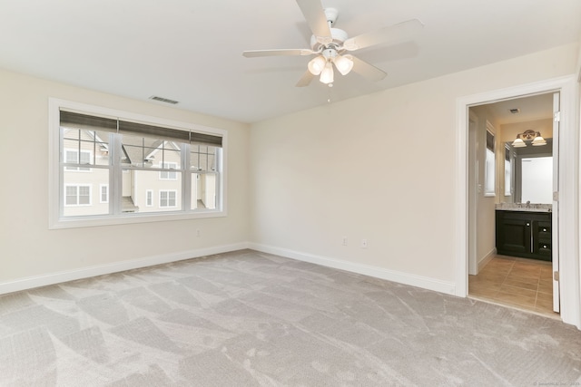 spare room featuring light colored carpet, a ceiling fan, visible vents, a sink, and baseboards