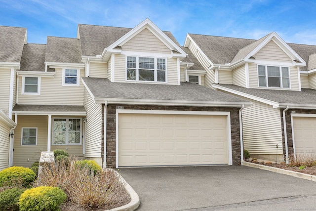view of property featuring an attached garage, a shingled roof, aphalt driveway, and stone siding