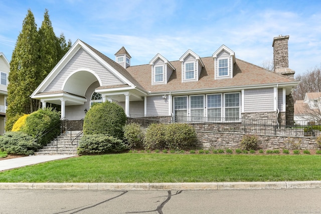 cape cod home with a chimney, a shingled roof, a front yard, and stone siding