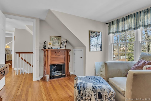 living area featuring baseboards, a fireplace with raised hearth, and light wood-style floors