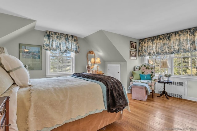 bedroom featuring radiator, multiple windows, lofted ceiling, and wood finished floors
