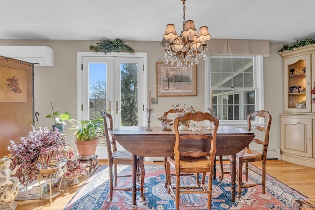dining room with an inviting chandelier, french doors, a wall mounted air conditioner, and light wood-type flooring