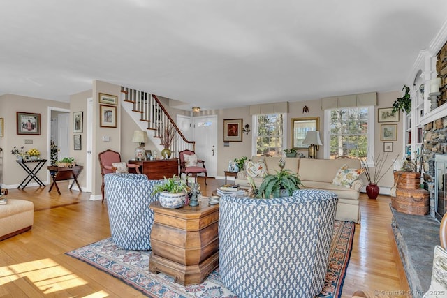 living area featuring stairway, a stone fireplace, a baseboard radiator, light wood-style flooring, and baseboards