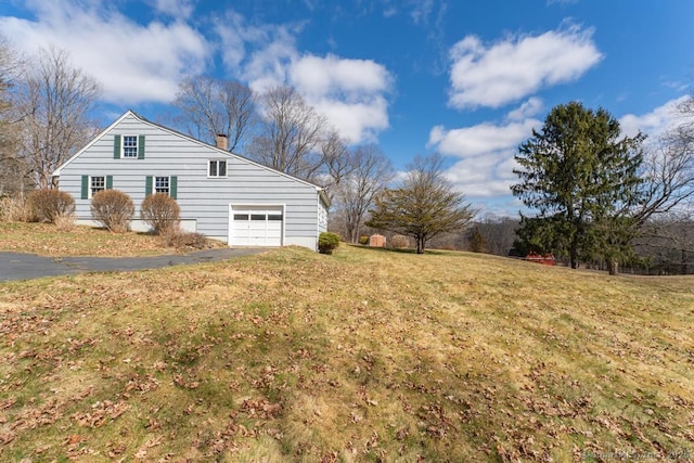 view of side of home featuring aphalt driveway, a chimney, and a yard